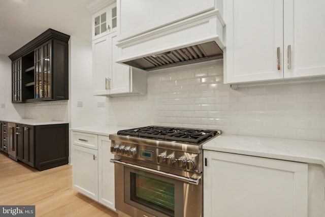 kitchen with backsplash, high end stainless steel range, light hardwood / wood-style flooring, custom range hood, and light stone counters