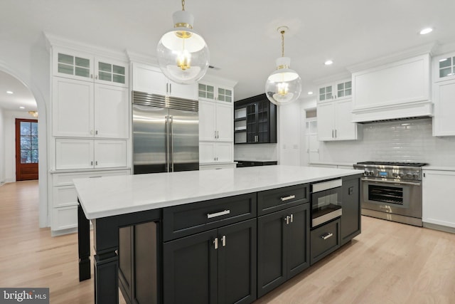 kitchen with tasteful backsplash, a center island, light hardwood / wood-style floors, decorative light fixtures, and built in appliances