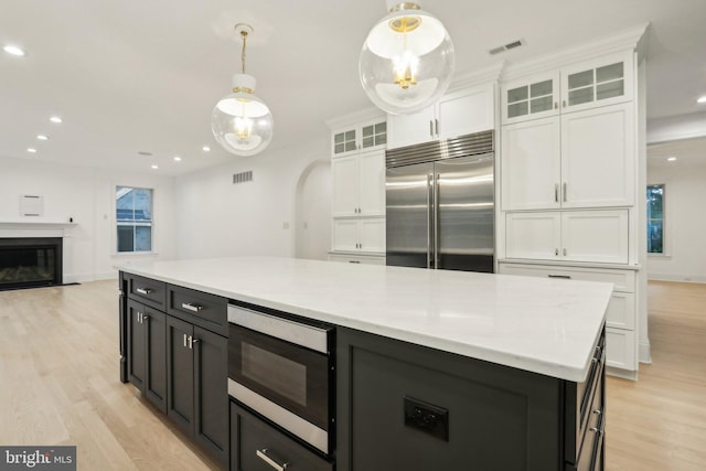 kitchen with built in appliances, decorative light fixtures, light wood-type flooring, and white cabinetry