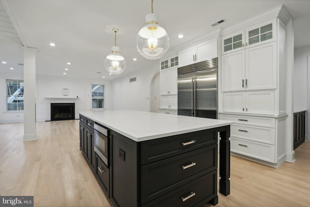 kitchen with built in appliances, hanging light fixtures, light hardwood / wood-style flooring, a center island, and white cabinets