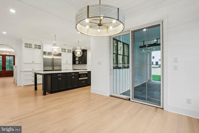 interior space with stainless steel built in refrigerator, white cabinetry, light wood-type flooring, a notable chandelier, and decorative light fixtures