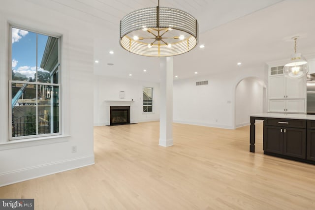 unfurnished living room featuring an inviting chandelier and light hardwood / wood-style flooring