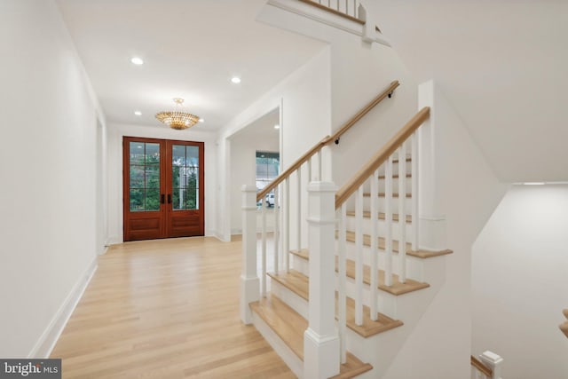 entryway with light hardwood / wood-style flooring, french doors, and a notable chandelier