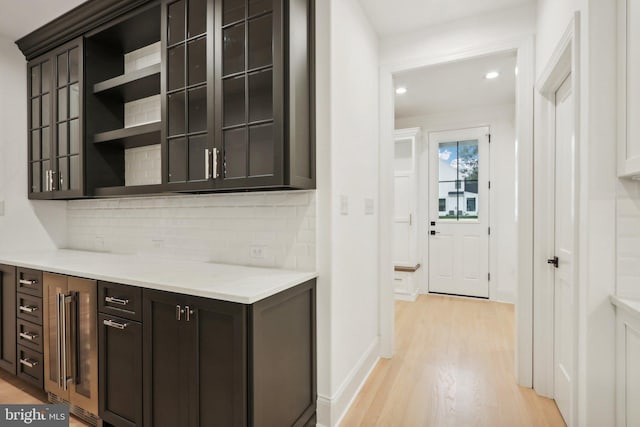 bar featuring wine cooler, dark brown cabinetry, tasteful backsplash, and light wood-type flooring