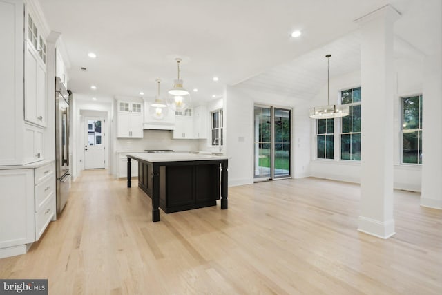 kitchen with white cabinets, a wealth of natural light, decorative light fixtures, and a large island with sink