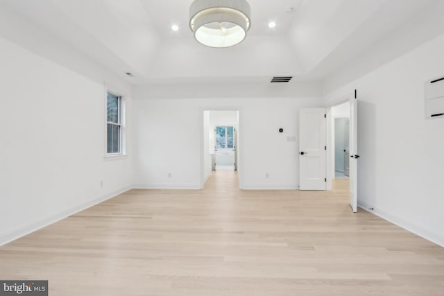 unfurnished room with light hardwood / wood-style floors and a tray ceiling