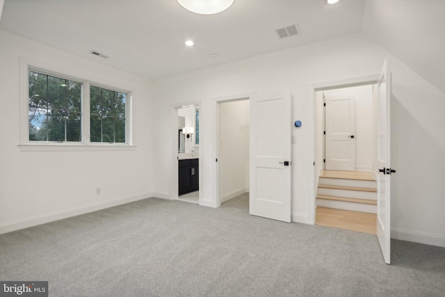 unfurnished bedroom featuring light carpet, lofted ceiling, and ensuite bath