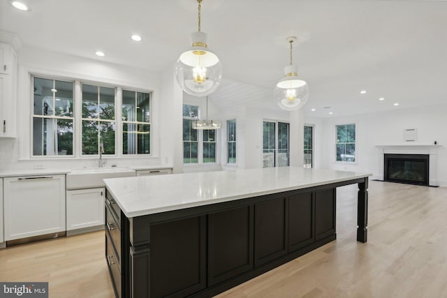 kitchen with white cabinets, hanging light fixtures, a kitchen island, light stone countertops, and light hardwood / wood-style floors