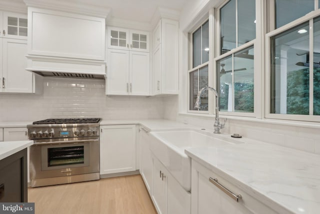 kitchen with light hardwood / wood-style flooring, high end range, sink, white cabinetry, and light stone counters