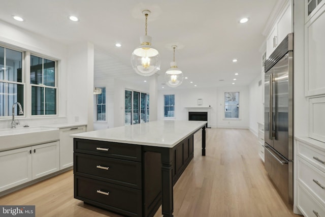 kitchen featuring white cabinetry, stainless steel built in refrigerator, hanging light fixtures, and a kitchen island