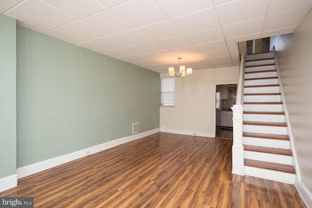 unfurnished room featuring a drop ceiling, a notable chandelier, and dark wood-type flooring