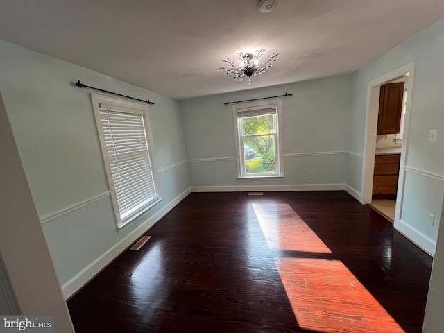 unfurnished room with dark wood-type flooring and a chandelier