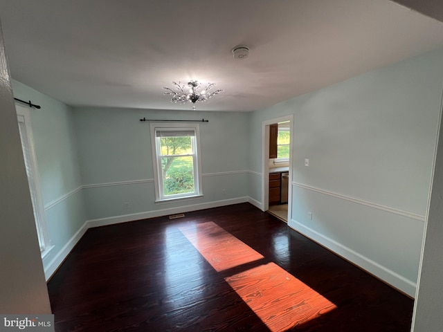 spare room with dark wood-type flooring and a chandelier