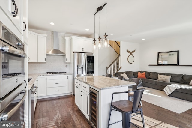 kitchen featuring wall chimney range hood, appliances with stainless steel finishes, dark hardwood / wood-style floors, beverage cooler, and a center island