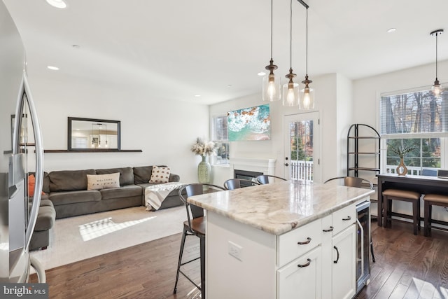 kitchen featuring a kitchen island, white cabinetry, dark hardwood / wood-style flooring, pendant lighting, and light stone countertops