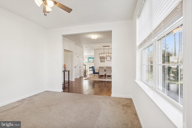 carpeted spare room featuring ceiling fan with notable chandelier