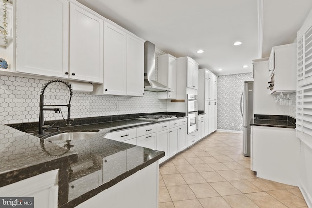 kitchen featuring dark stone countertops, white cabinetry, sink, and wall chimney range hood