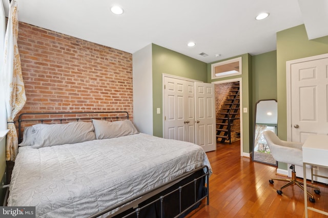 bedroom featuring a closet, wood-type flooring, and brick wall