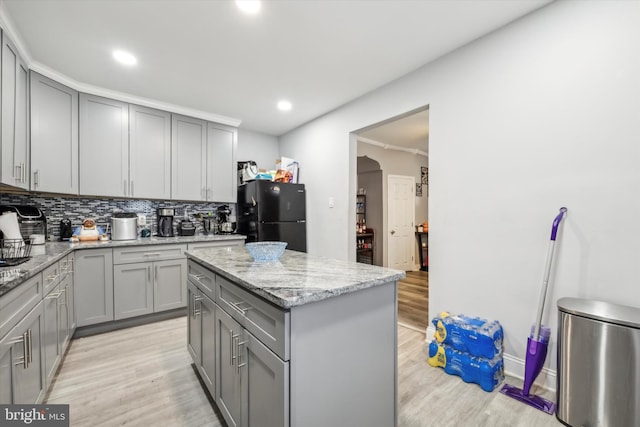 kitchen with decorative backsplash, black refrigerator, light stone countertops, a center island, and light wood-type flooring