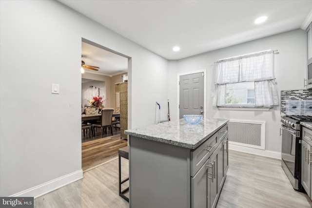 kitchen with light hardwood / wood-style flooring, stainless steel range, gray cabinetry, ornamental molding, and a center island