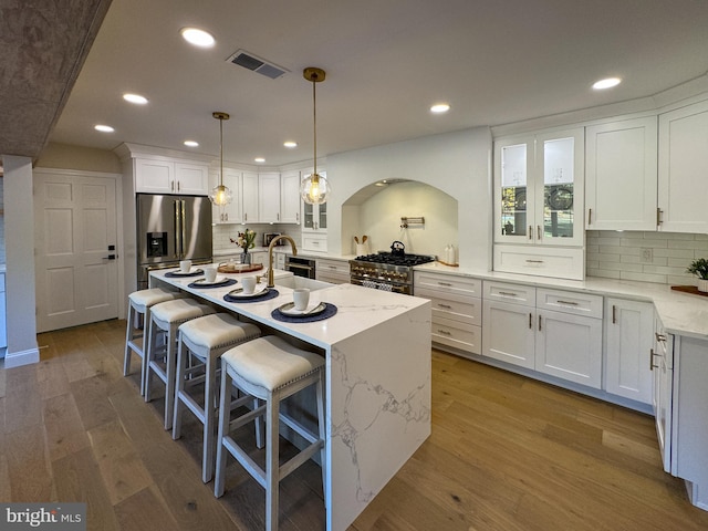 kitchen with a center island with sink, white cabinets, pendant lighting, appliances with stainless steel finishes, and light hardwood / wood-style floors