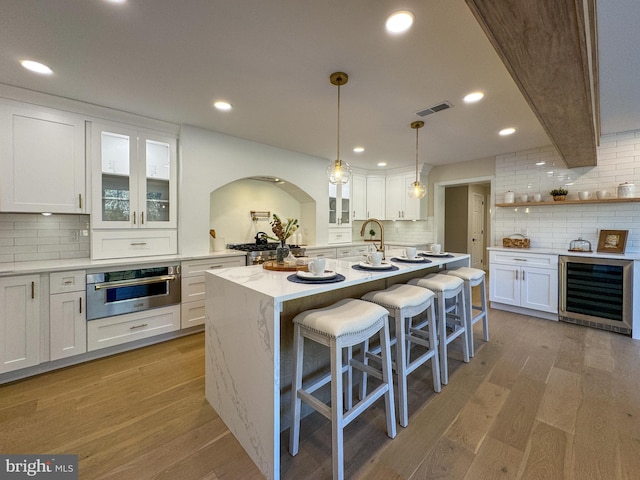 kitchen with white cabinetry, wine cooler, oven, and light wood-type flooring