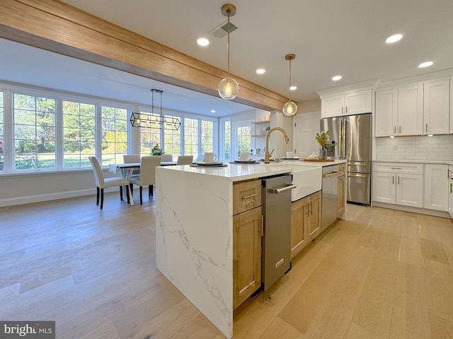 kitchen featuring white cabinets, stainless steel appliances, hanging light fixtures, and an island with sink