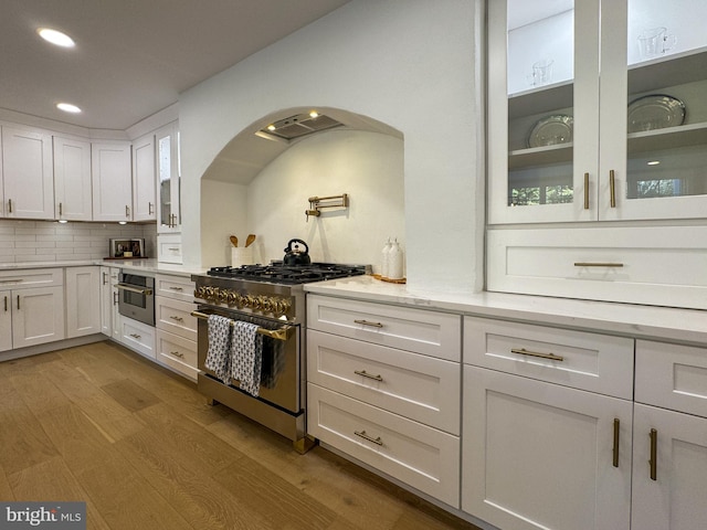 kitchen with decorative backsplash, light hardwood / wood-style flooring, white cabinetry, appliances with stainless steel finishes, and light stone counters