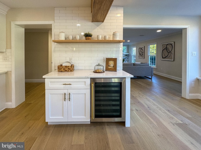 bar with wine cooler, decorative backsplash, white cabinetry, and light wood-type flooring