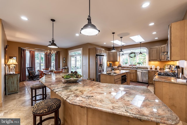 kitchen with a spacious island, light stone countertops, a kitchen bar, stainless steel appliances, and a sink