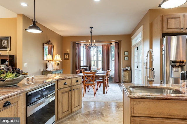 kitchen with a sink, appliances with stainless steel finishes, light stone countertops, a chandelier, and hanging light fixtures