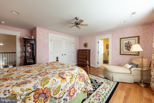 bedroom with visible vents, a ceiling fan, wood finished floors, a closet, and wallpapered walls