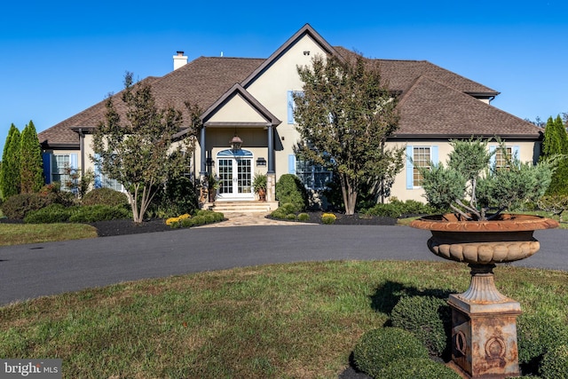 view of front of property featuring french doors, roof with shingles, a chimney, and stucco siding