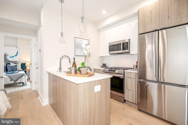 kitchen with appliances with stainless steel finishes, sink, pendant lighting, white cabinets, and light hardwood / wood-style floors