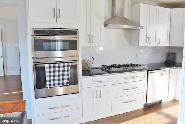 kitchen featuring decorative backsplash, wall chimney range hood, hardwood / wood-style flooring, white cabinetry, and appliances with stainless steel finishes