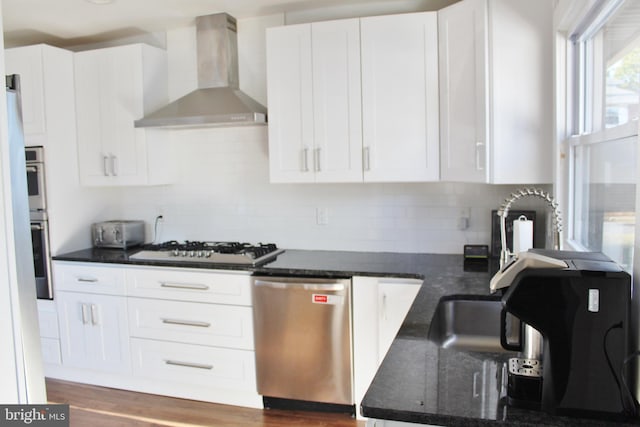 kitchen with white cabinets, stainless steel dishwasher, dark stone counters, white gas cooktop, and wall chimney exhaust hood