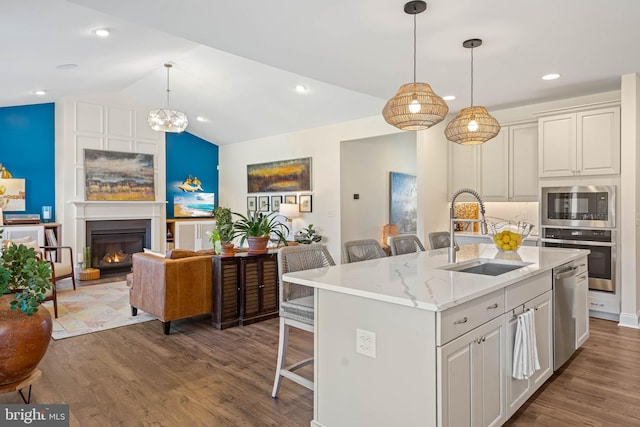 kitchen with light stone countertops, sink, an island with sink, stainless steel appliances, and a breakfast bar