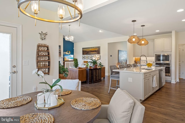 kitchen featuring dark wood-type flooring, an island with sink, hanging light fixtures, stainless steel appliances, and an inviting chandelier