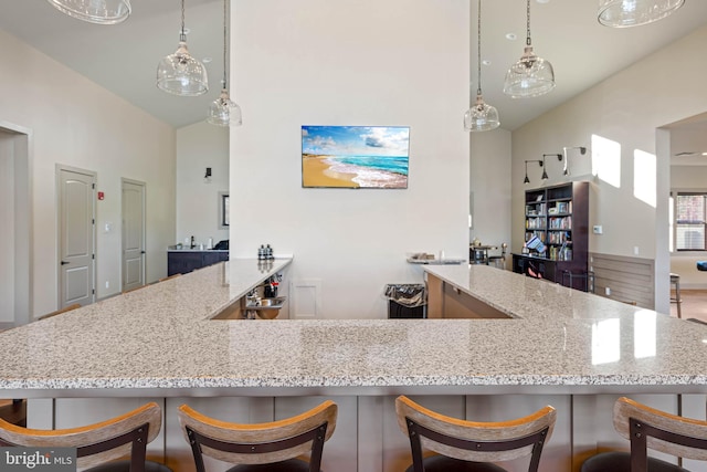 kitchen featuring lofted ceiling, a breakfast bar area, kitchen peninsula, pendant lighting, and light stone counters