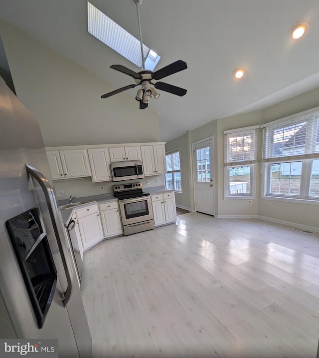 kitchen featuring appliances with stainless steel finishes, a skylight, ceiling fan, light hardwood / wood-style flooring, and white cabinets