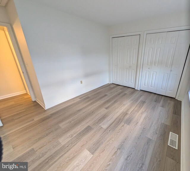 unfurnished bedroom with two closets and light hardwood / wood-style flooring