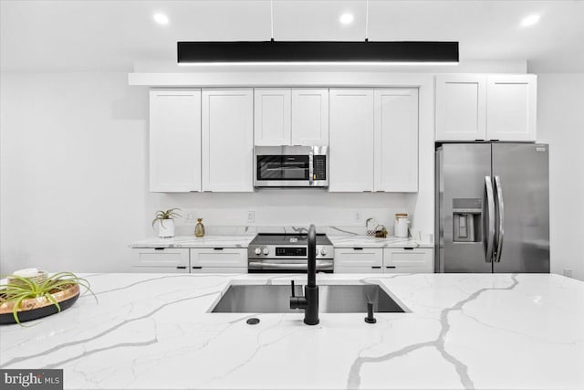 kitchen featuring appliances with stainless steel finishes, white cabinetry, and light stone counters