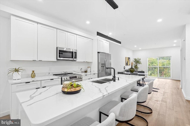 kitchen with sink, pendant lighting, a kitchen island with sink, appliances with stainless steel finishes, and light wood-type flooring