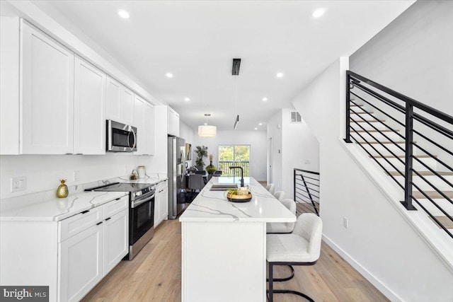 kitchen featuring light wood-type flooring, light stone counters, stainless steel appliances, a kitchen island, and a breakfast bar area