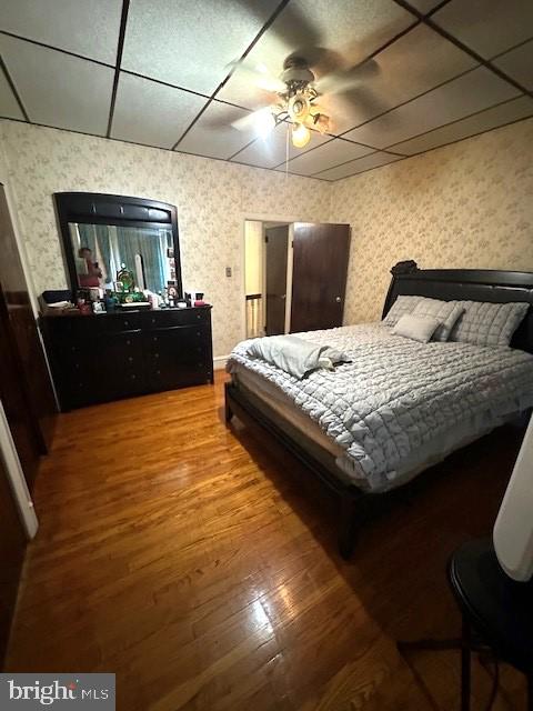 bedroom featuring a drop ceiling, hardwood / wood-style flooring, and ceiling fan