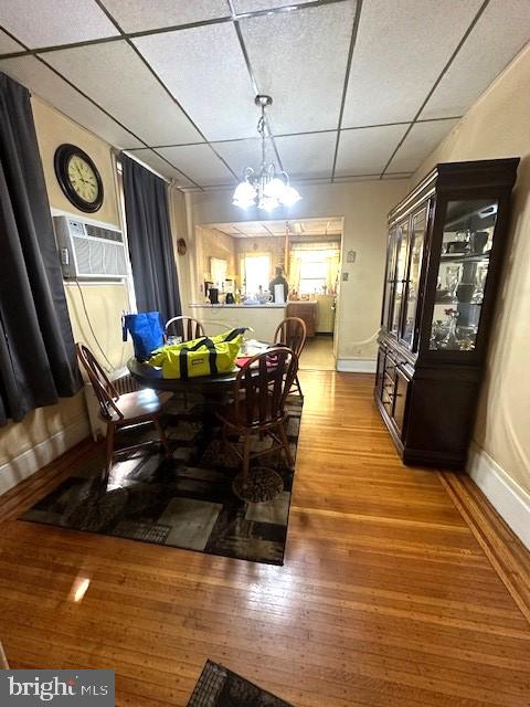 dining area with a wall mounted air conditioner, a drop ceiling, a chandelier, and light wood-type flooring