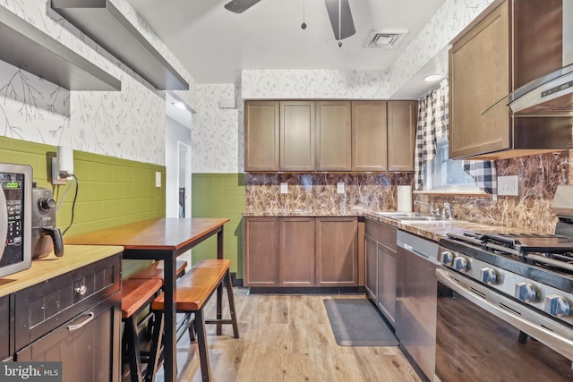 kitchen featuring ceiling fan, sink, wall chimney exhaust hood, stainless steel appliances, and light wood-type flooring