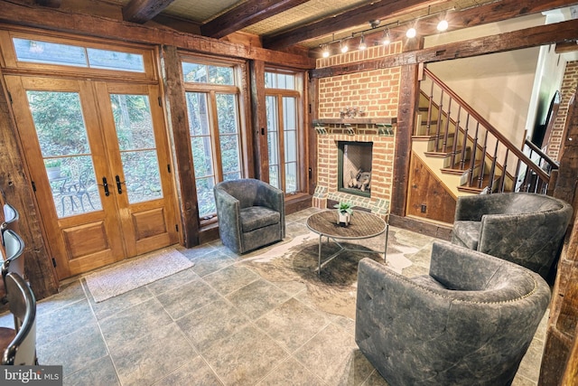 living room featuring french doors, beamed ceiling, and a brick fireplace