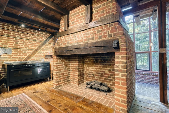 interior space with rail lighting, brick wall, beamed ceiling, and light wood-type flooring