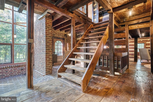 stairway with hardwood / wood-style floors, beam ceiling, wooden ceiling, and brick wall